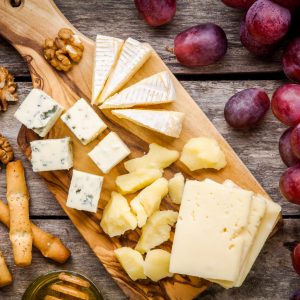 Cheese plate: Emmental, Camembert cheese, blue cheese, bread sticks, walnuts, grapes on wooden table